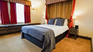 A hotel room with a large bed, a bench along the window, and a nightstand with a lamp.