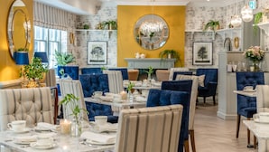 A dining area with round tables, blue upholstered chairs, and a chandelier. - Villiers Hotel (Buckingham)