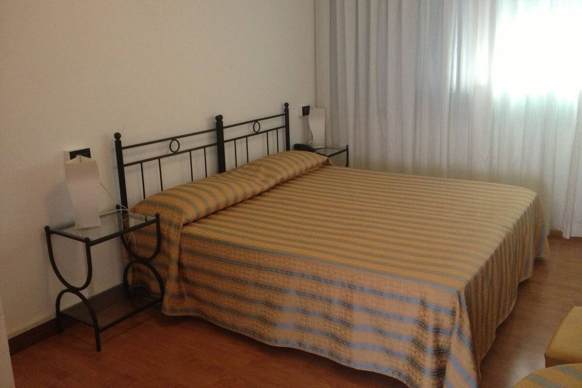 A single bed with a striped bedspread in a room with a metal headboard and a glass bedside table.
