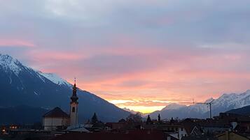 A town with a prominent church tower, snow-capped mountains in the background, and a sunset sky.