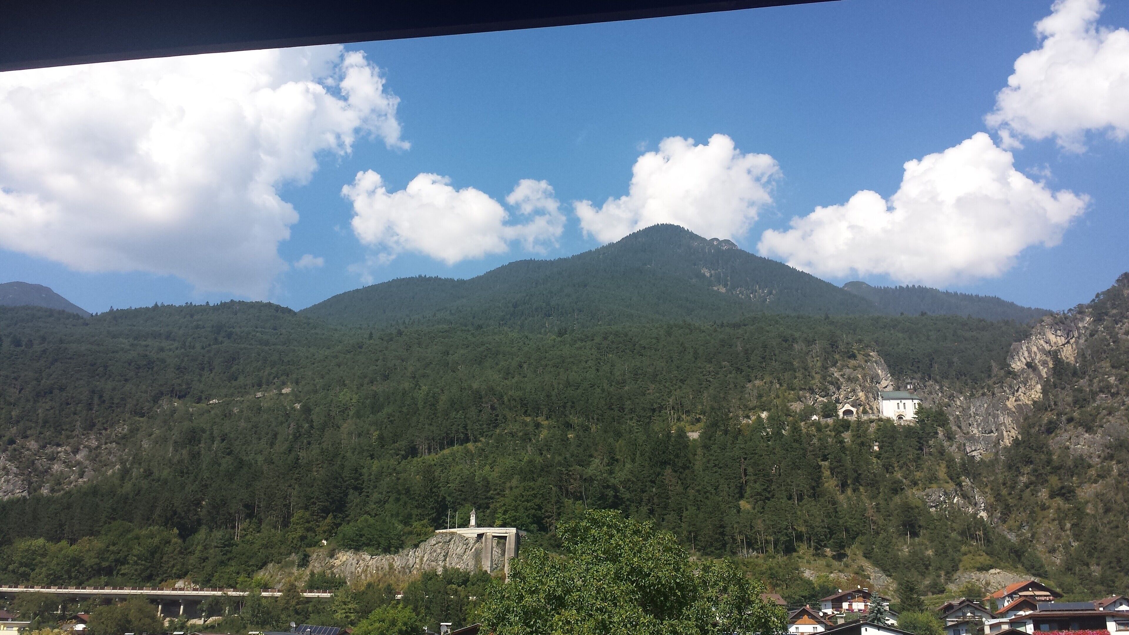 A mountainous landscape with a bridge, a white building, and dense forest.