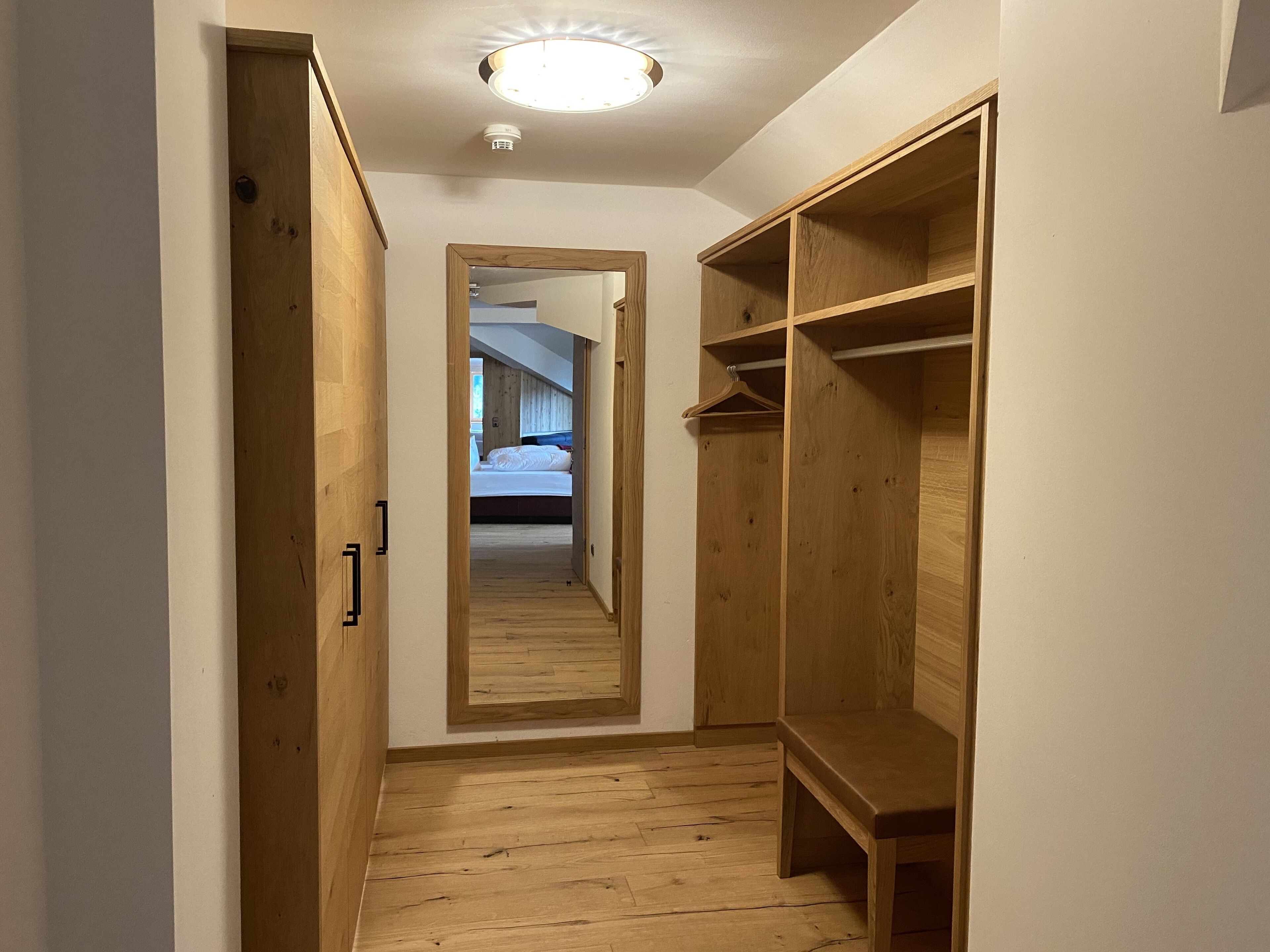 Un pasillo estrecho con suelo de madera y una puerta de armario espejada.