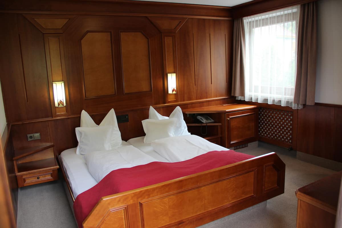 A hotel room with a large bed, wooden headboard, bedside tables, a desk, and a window with curtains.