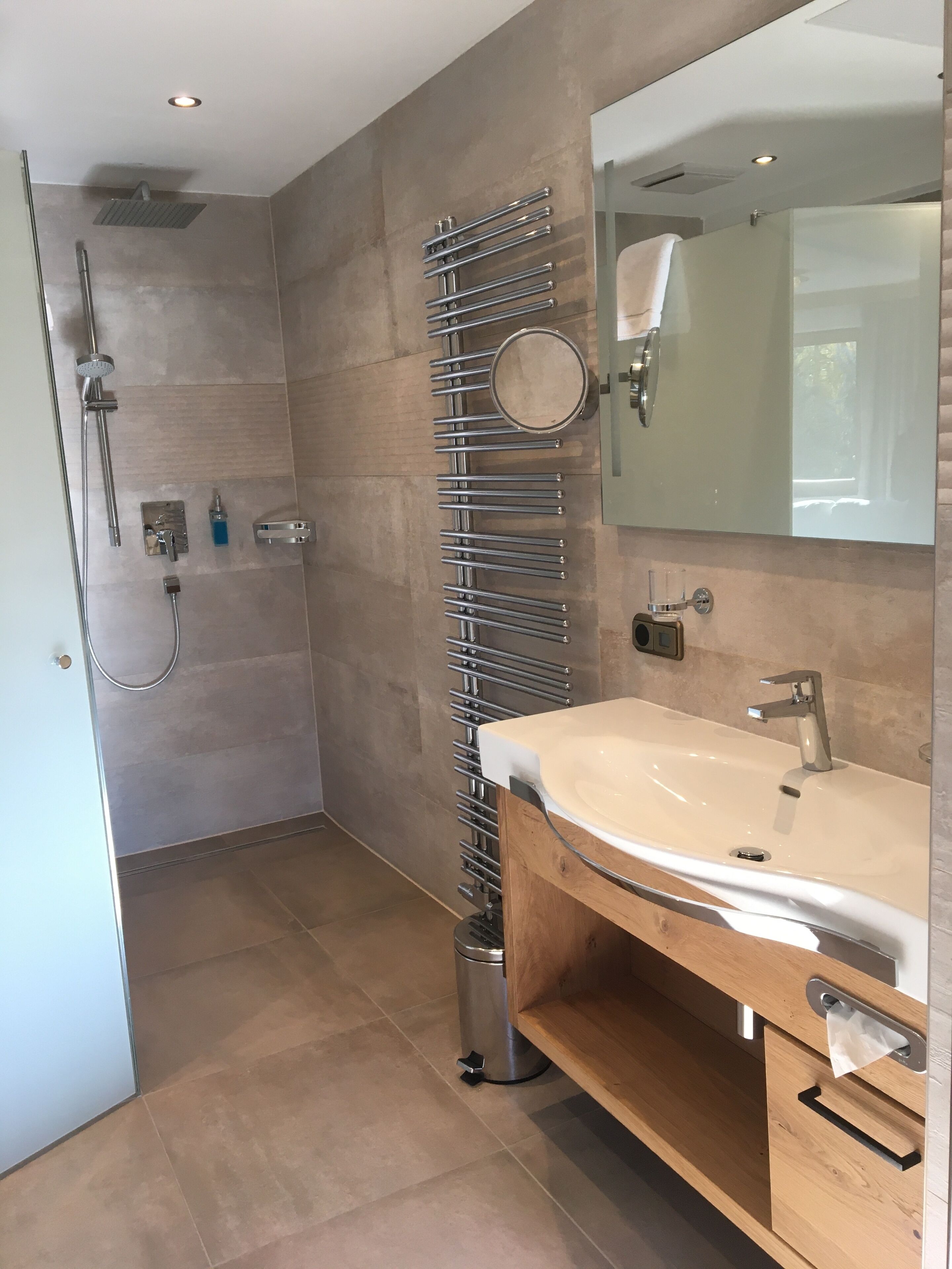 A modern bathroom with a walk-in shower, a large mirror, and a wooden vanity with a sink.