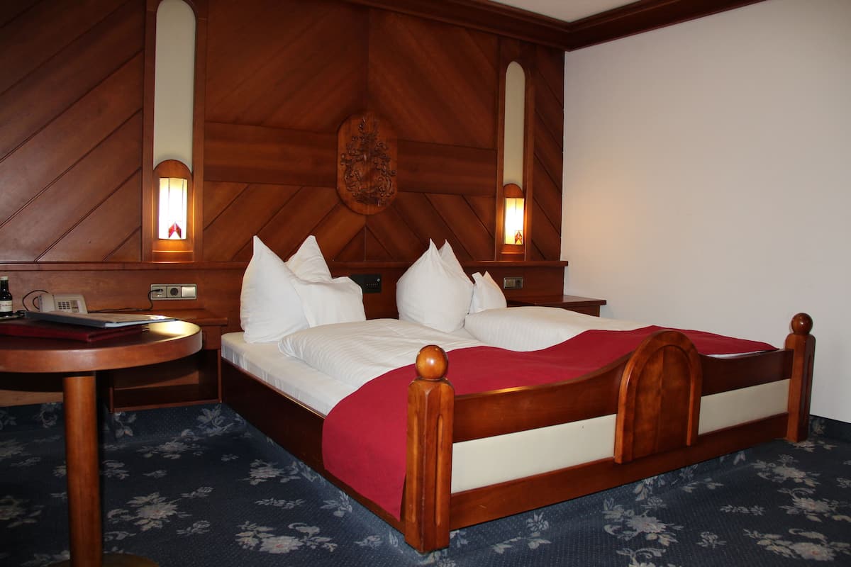 A hotel room with a wooden headboard, a round bedside table, a bed with white bedding, and two wall-mounted lamps.