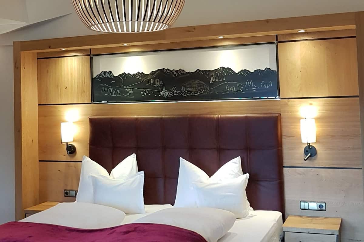 A bedroom with a large bed, wooden ceiling beams, a wall-mounted artwork, bedside lamps, and a nightstand.