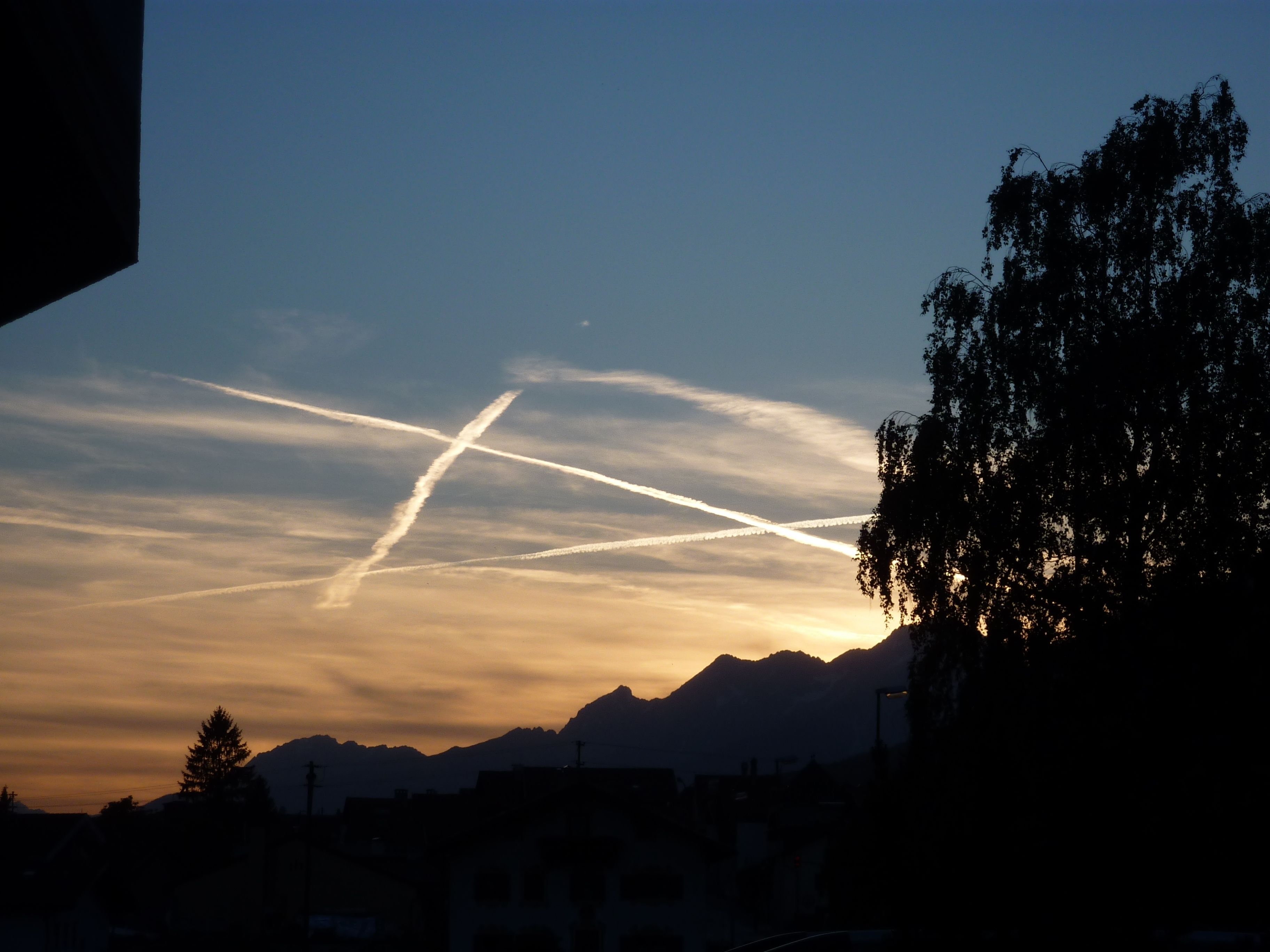 A sunset with mountains in the background and contrails in the sky.