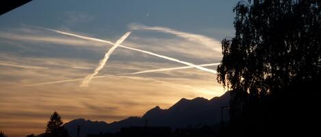 A sunset with mountains in the background and contrails in the sky.