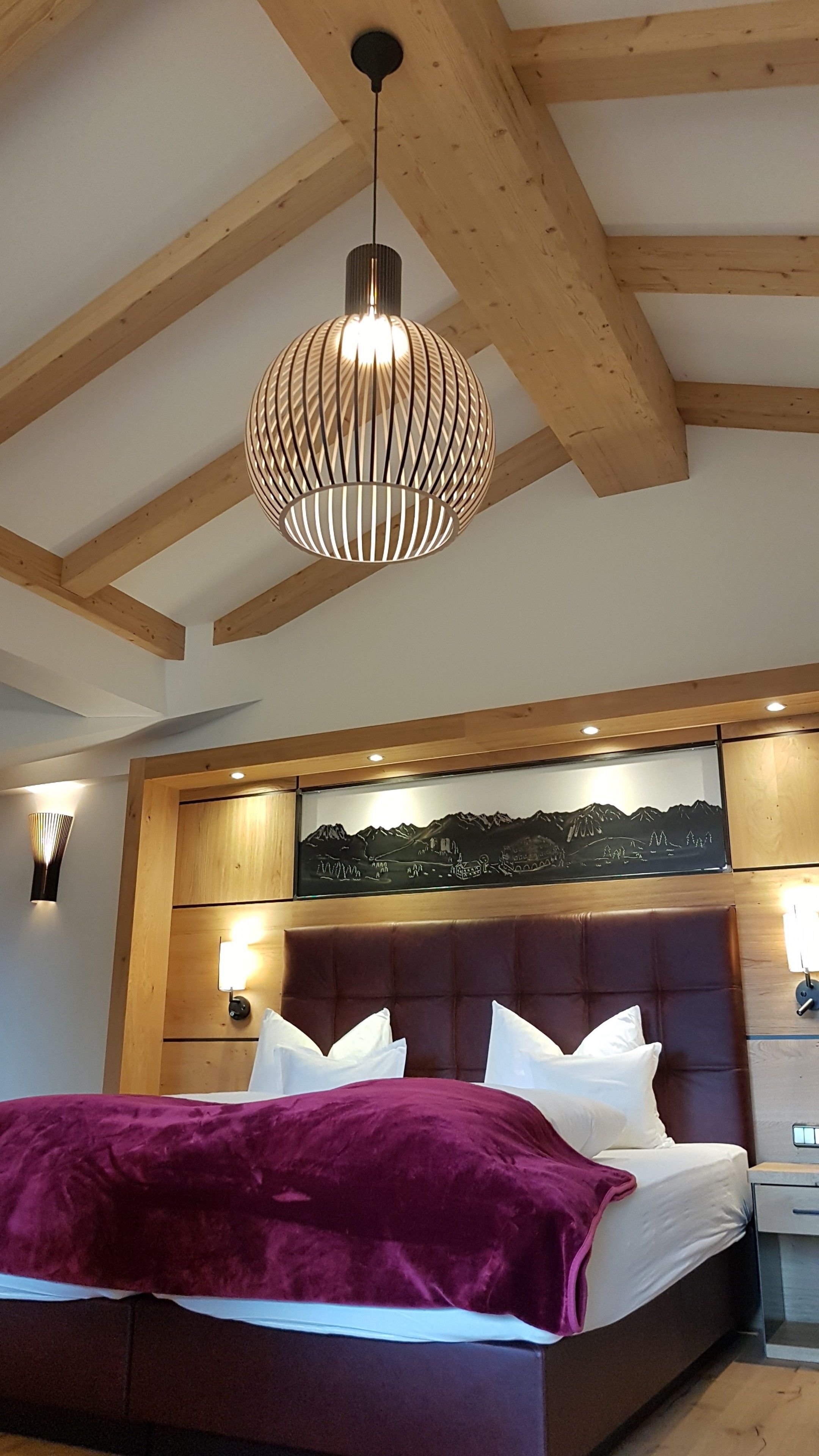 Une chambre dotée d’un grand lit, d’un plafond en bois et d’une œuvre d’art fixée au mur, représentant un paysage montagneux.