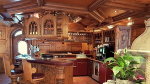 A wooden bar area with stools, a kitchen with a dishwasher, and a potted plant on a table. - Hotel Tyrolis (Zirl)