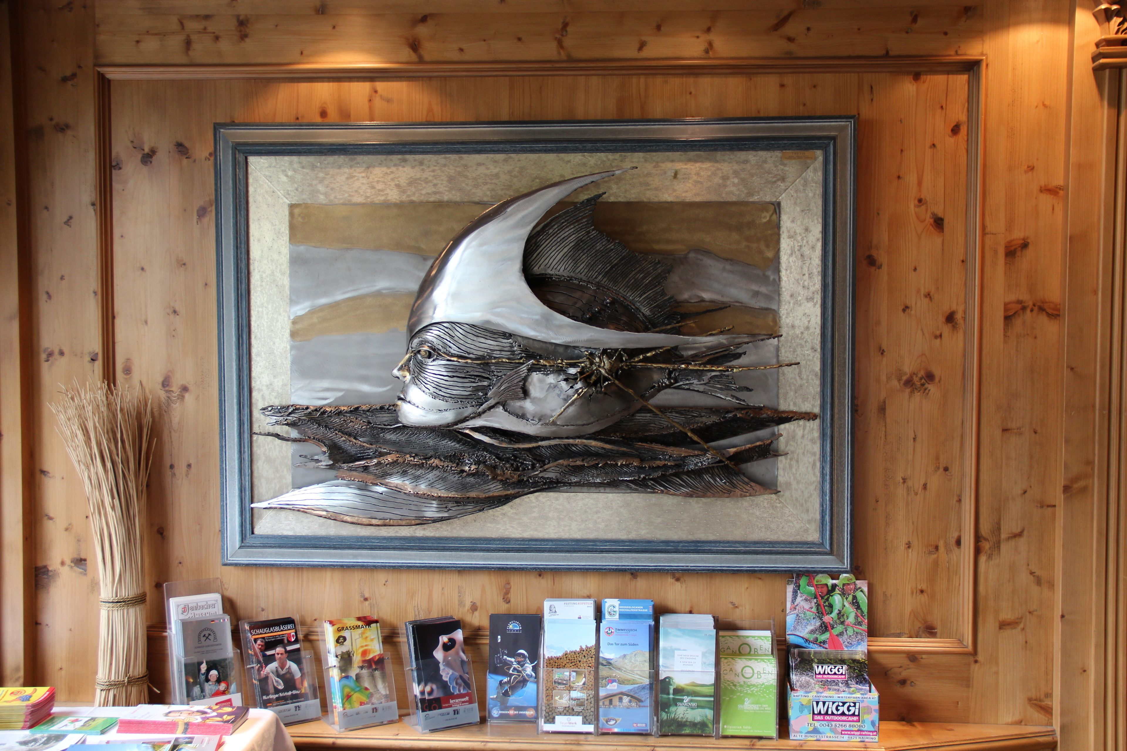 A framed artwork of a fish on a wall, a wooden shelf with books and magazines, and a vase with reeds.