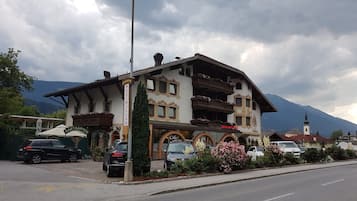 Een traditioneel gebouw in Alpenstijl met een restaurant, café en bar op de begane grond, omringd door geparkeerde auto's en weelderige begroeiing.