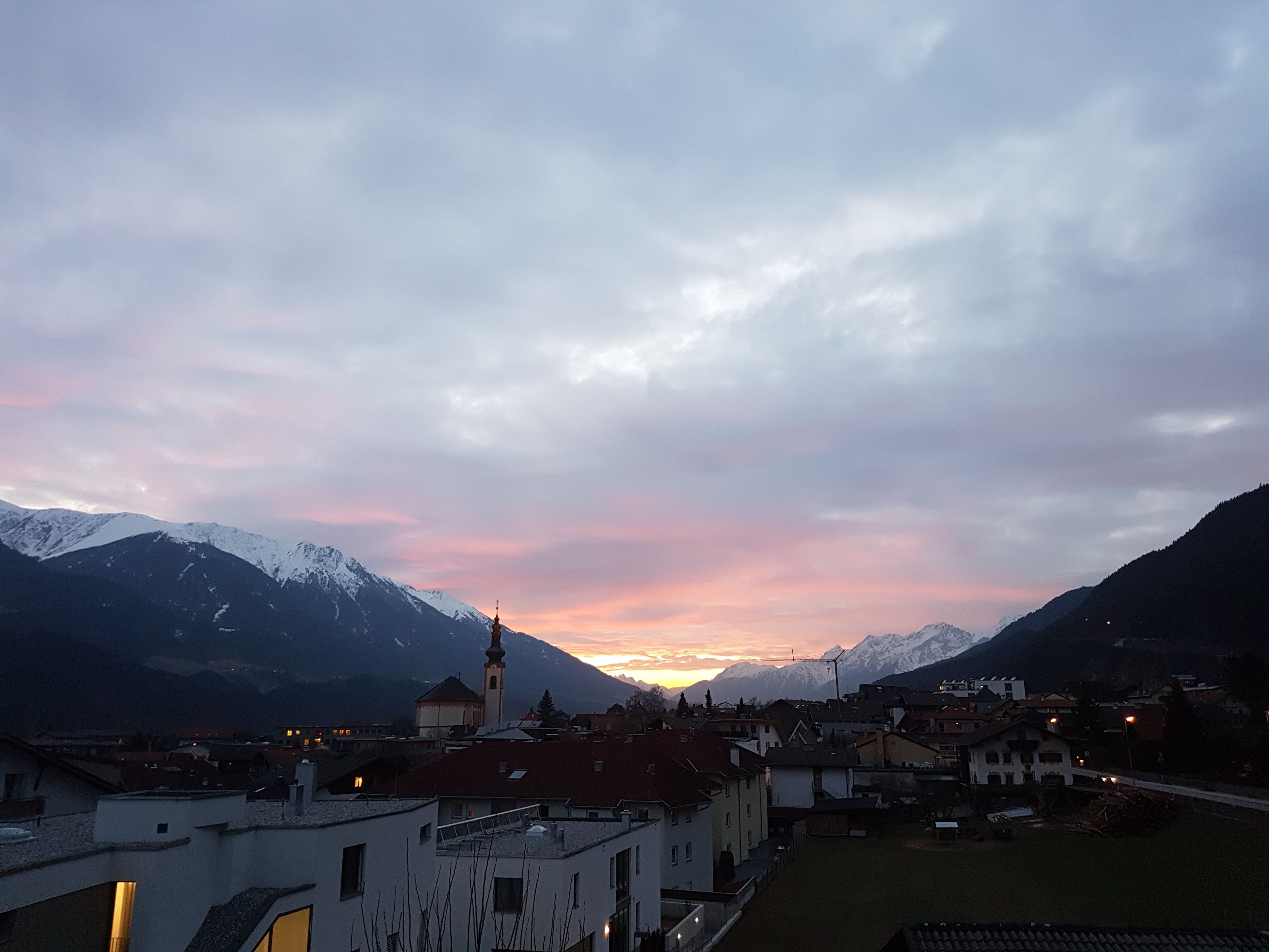 Une ville avec des bâtiments et une église, entourée de montagnes et illuminée par le ciel au coucher du soleil.