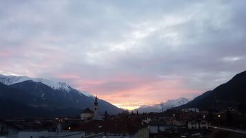 Une ville avec des bâtiments et une église, entourée de montagnes et illuminée par le ciel au coucher du soleil.