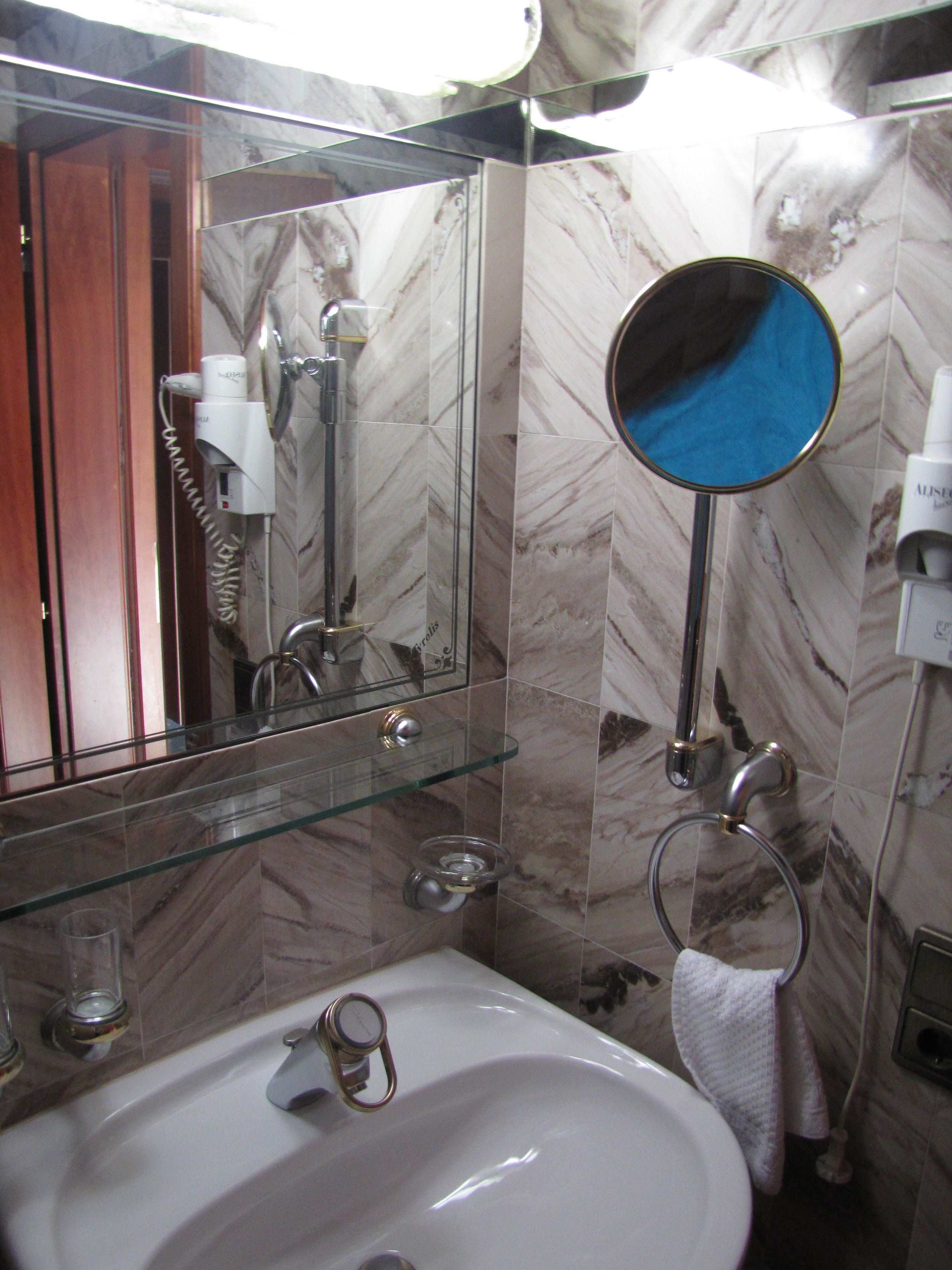 Un baño con repisa de vidrio, lavamanos, espejo y aro para toallas.