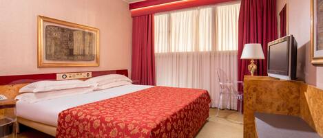 Una habitación de hotel con una cama grande, un escritorio con una silla, un televisor y un cuadro en la pared.