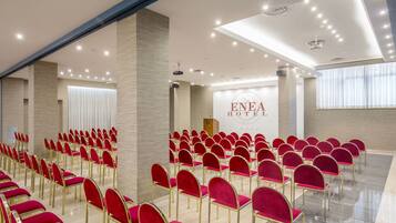 Un salón de conferencias de hotel con filas de sillas rojas y un atril al fondo.