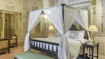 Een hemelbed met witte draperingen, een groene bank, een klein tafeltje met een lamp en decoratieve muurversieringen.
