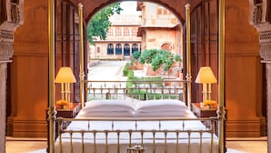 A bed with a green bedspread and a tray of tea set, a red and black patterned rug, and a view of a courtyard with a building and greenery. - The Laxmi Niwas Palace (Bikaner)