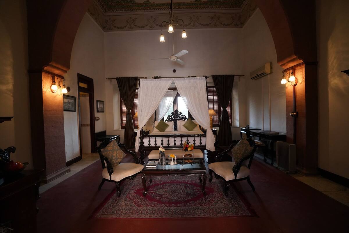 Une chambre de style traditionnel, dotée d’un lit à baldaquin, de deux fauteuils, d’une table basse et d’un lustre.