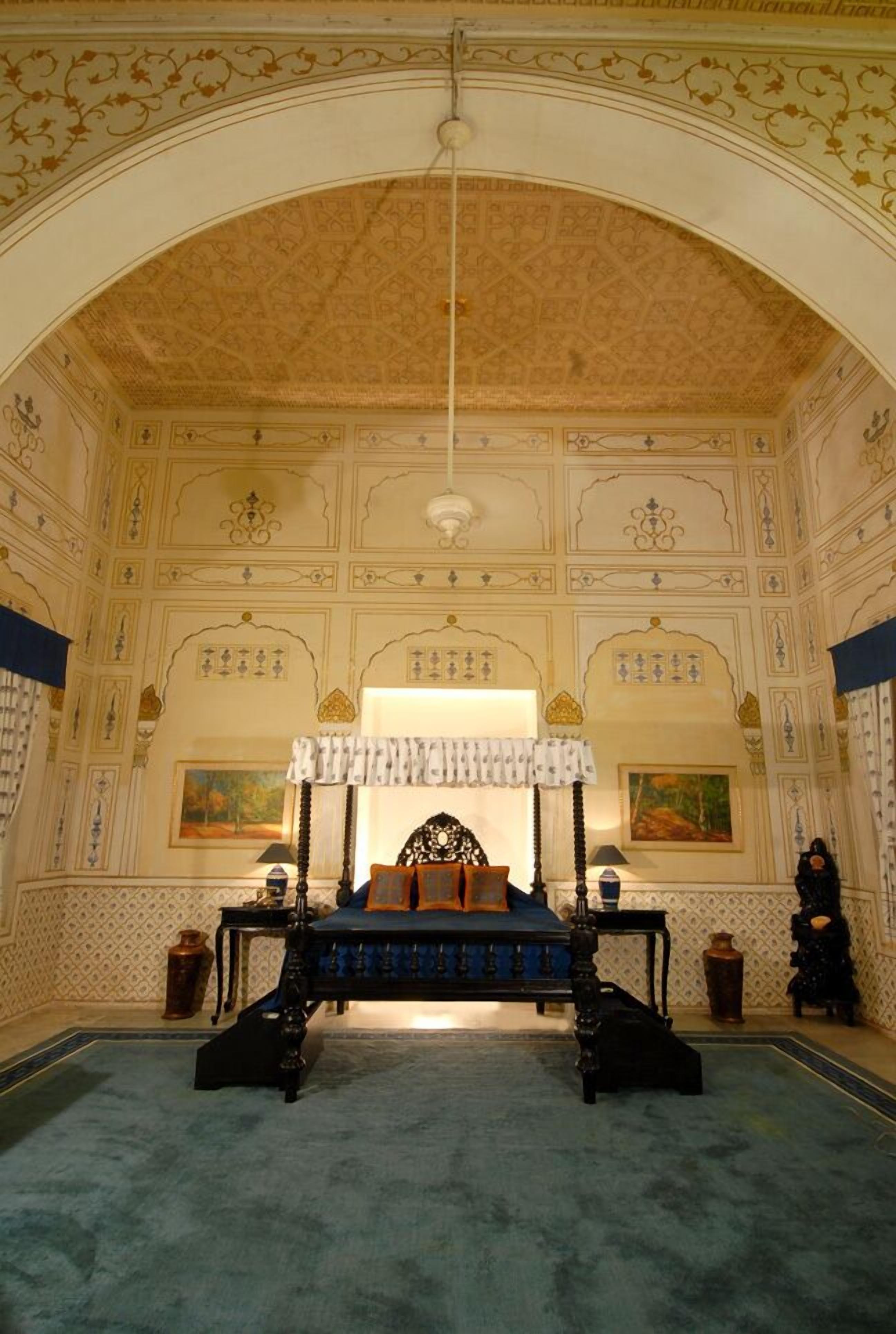 A room with a large bed, ornate ceiling, and patterned walls.