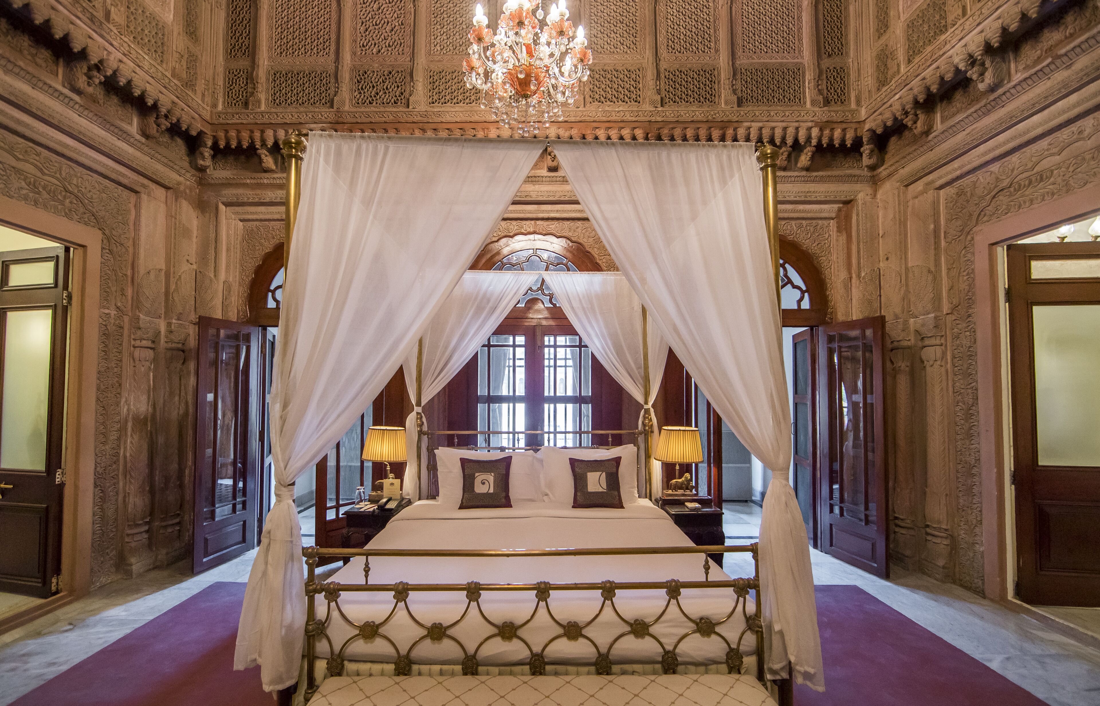 A four-poster bed with a canopy, ornate wall carvings, and a chandelier.