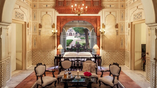 An opulent room with a large bed, ornate ceiling, and a view of a garden through an arched doorway. - The Laxmi Niwas Palace (Bikaner)