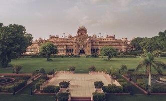 Un edificio grande e histórico con una cúpula central y varias cúpulas más pequeñas, rodeado de jardines y senderos bien cuidados.