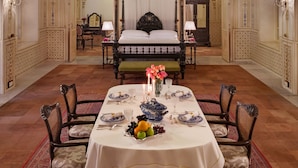 A luxurious room with an ornate ceiling, a four-poster bed, and a dining area with a table set for four. - The Laxmi Niwas Palace (Bikaner)