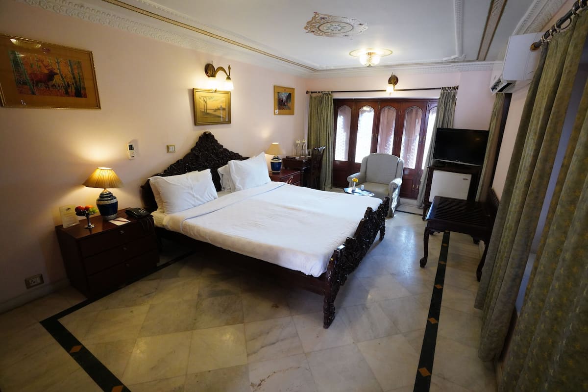 Une chambre d’hôtel avec un grand lit, un bureau avec une chaise, une télévision et une fenêtre avec des rideaux.