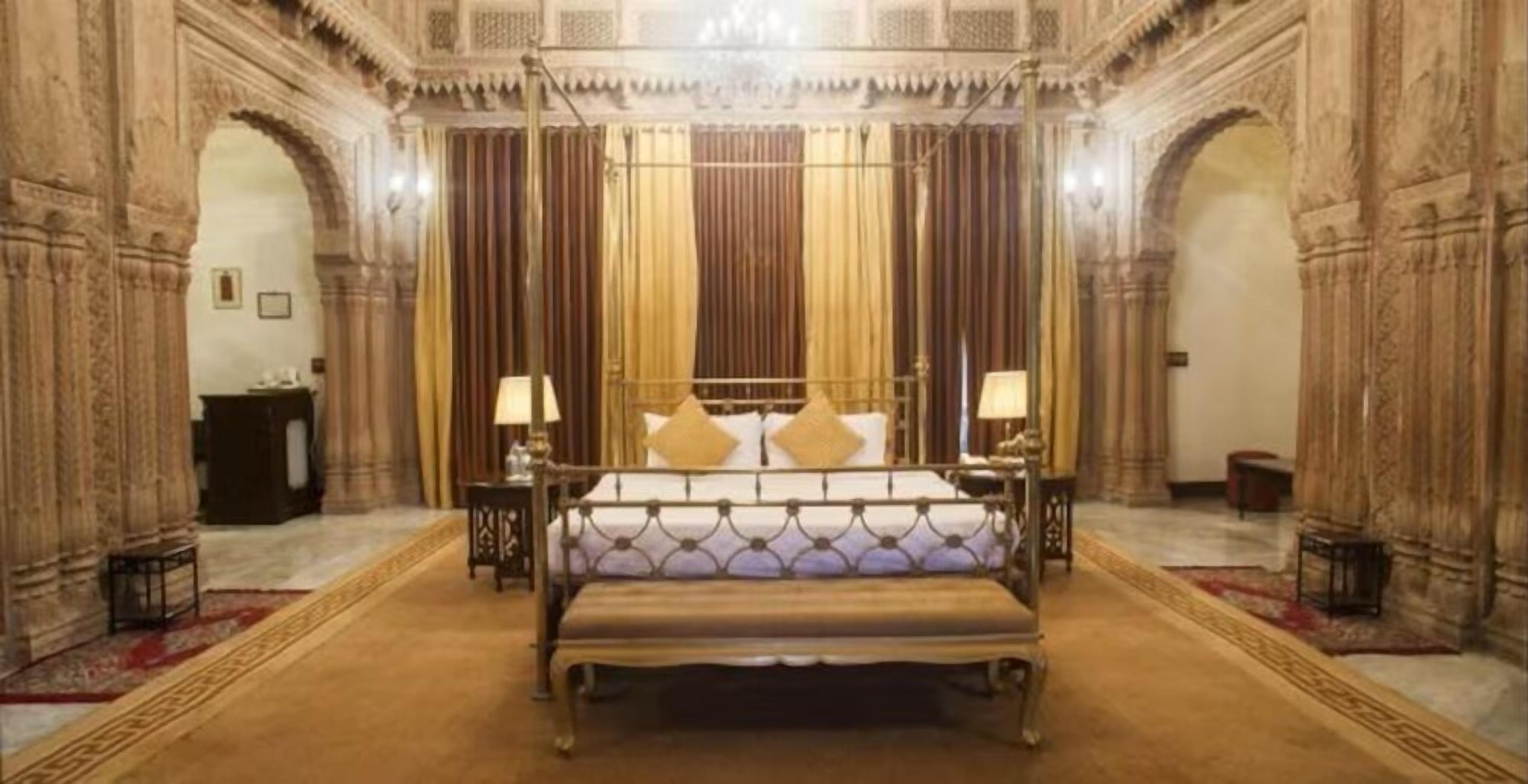 Une chambre à coucher luxueuse, dotée d’un grand lit, de rideaux richement décorés et de sculptures complexes sur les murs.