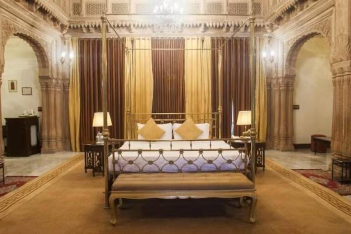 Une chambre à coucher luxueuse, dotée d’un grand lit, de rideaux richement décorés et de sculptures complexes sur les murs.