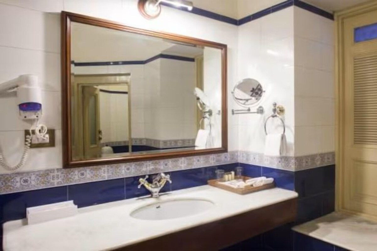Een badkamer met een wastafel, spiegel, handdoekrek en een deur met een handdoek eraan.