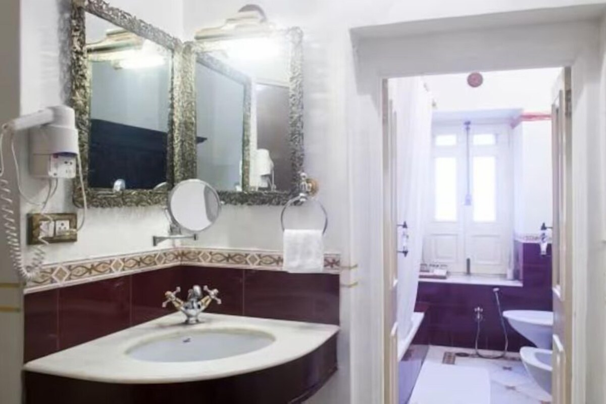 Een badkamer met een wastafel, twee spiegels, een toilet en een douche.