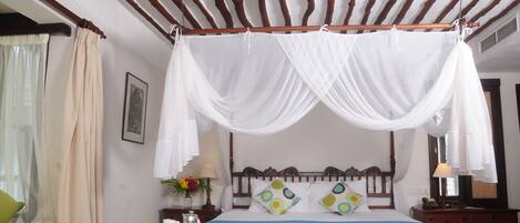 A room with a bed under a canopy, a small table with breakfast items, and a green chair.