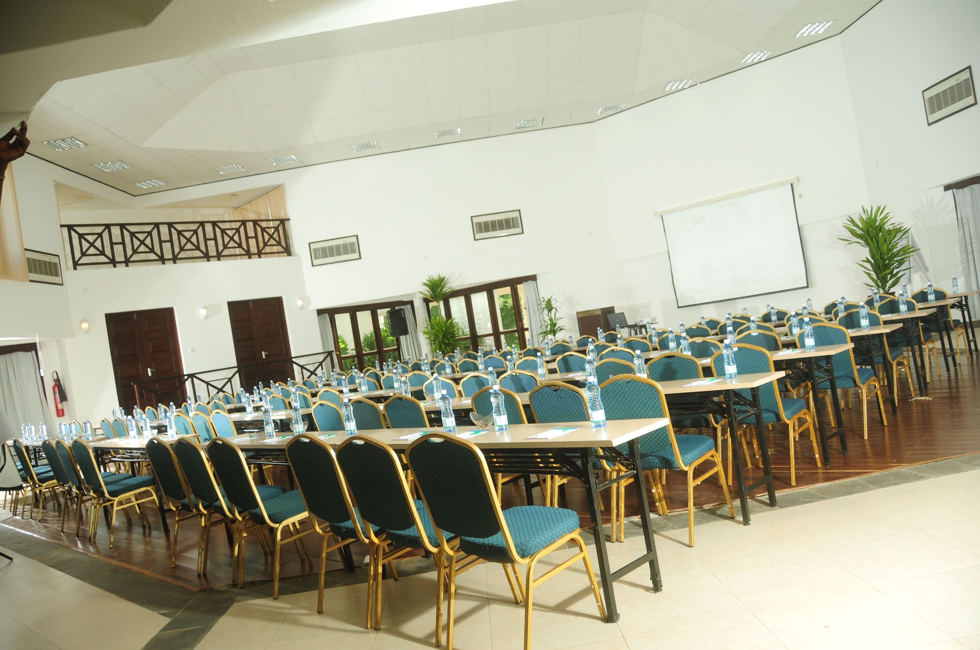 Une salle de conférence avec des rangées de tables et de chaises, un tableau blanc et une grande fenêtre donnant sur l’extérieur.