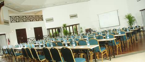 Un salón de conferencias con filas de mesas y sillas, una pizarra y un amplio ventanal con vistas al exterior.