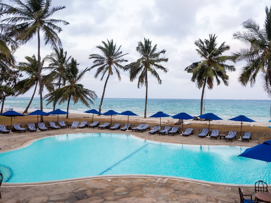 Un espace piscine aménagé avec des chaises longues et des parasols, des palmiers et une vue sur l’océan.