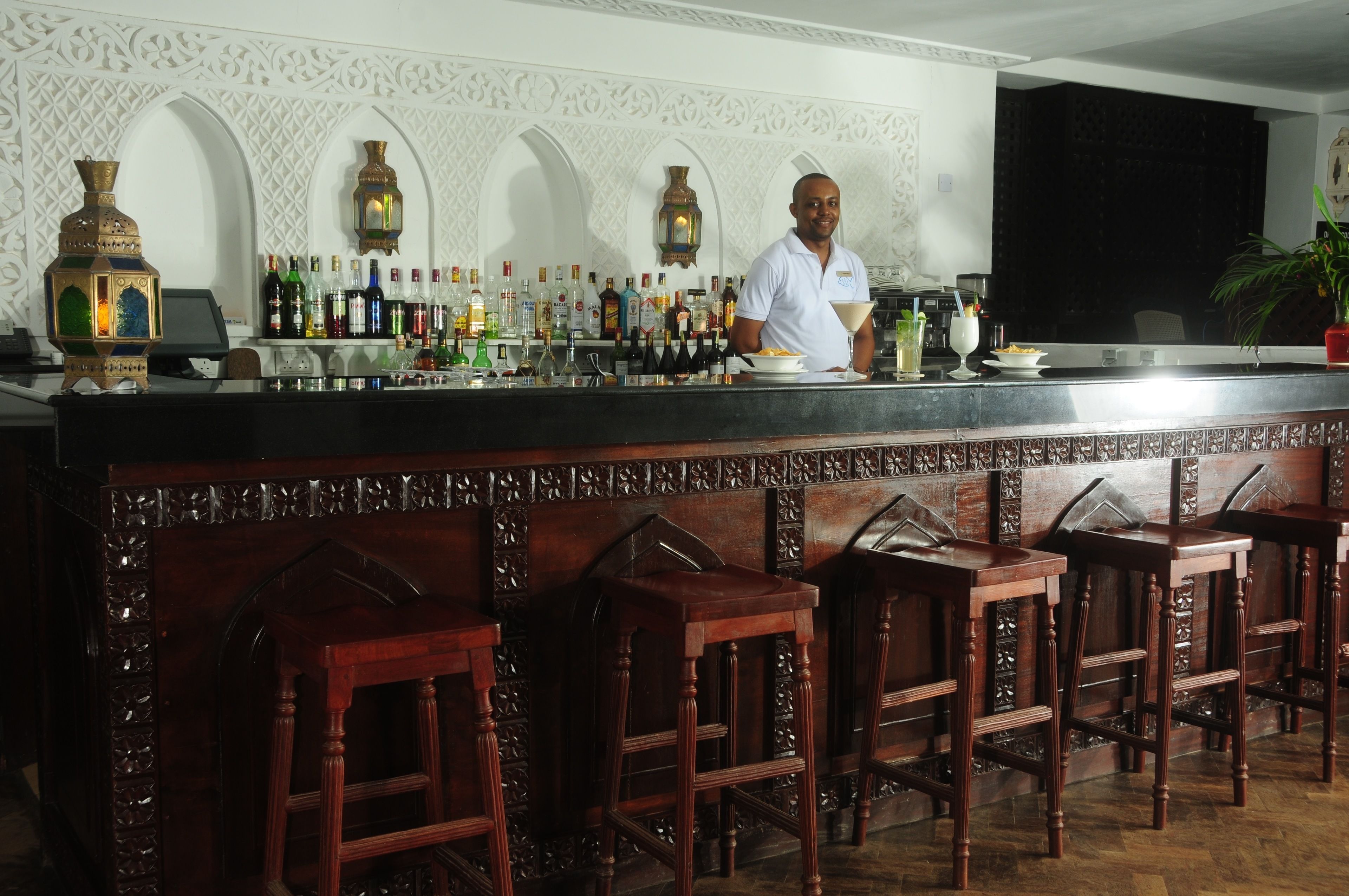 A bar area with a bartender, a variety of bottles, and ornate wall decorations.