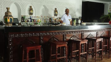 A bar area with a bartender, a variety of bottles, and ornate wall decorations.