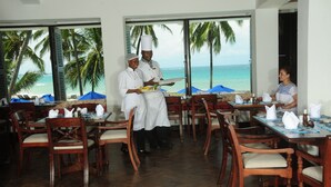 Un restaurante con mobiliario de madera y grandes ventanales con vistas a la playa.