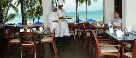A restaurant with wooden furniture and large windows overlooking a beach.