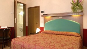 Habitación de hotel con cama, escritorio, silla, baño y estante en la pared con flores.