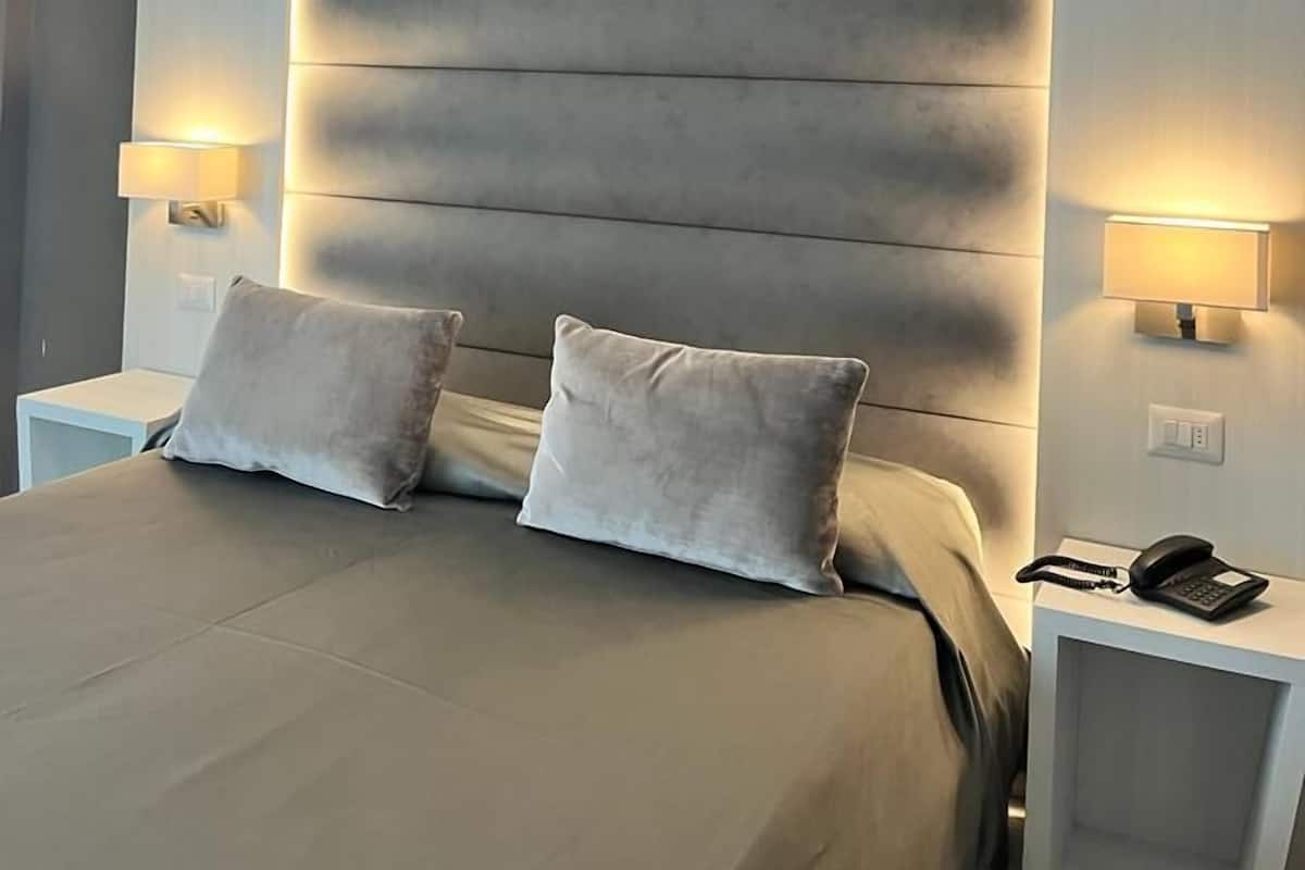 A modern hotel room with a large bed, two bedside tables, and a wall-mounted light fixture.