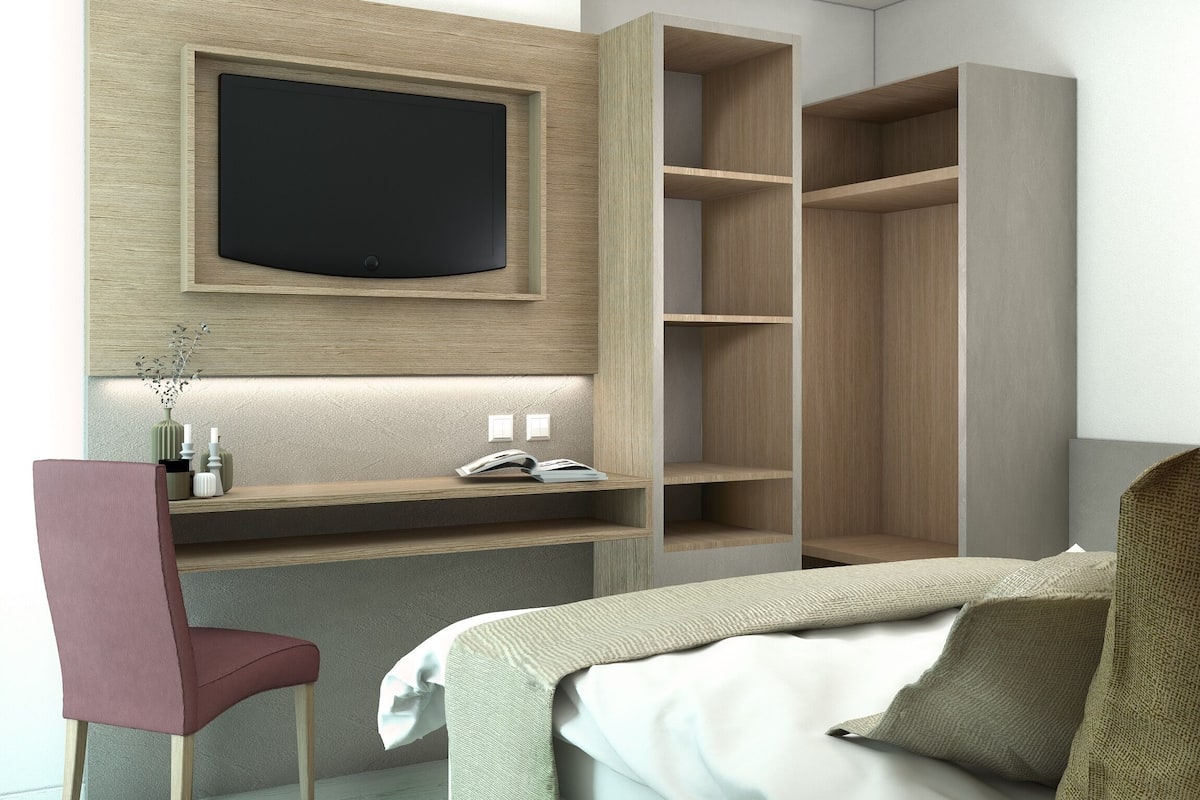 A modern hotel room with a bed, a desk, a chair, and built-in shelving.