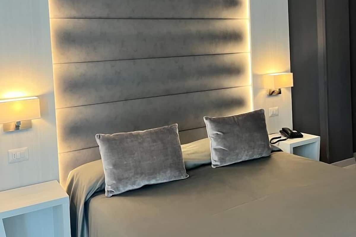 A modern bedroom with a large bed, two bedside tables, and a headboard with built-in lighting.