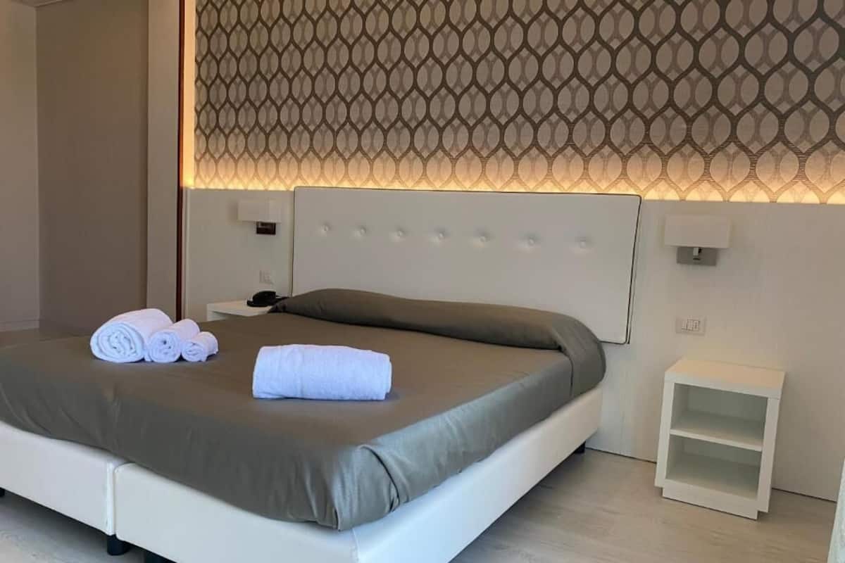 A modern hotel room with a neatly made bed, a bedside table, and a patterned wall.
