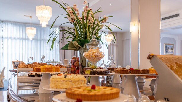 A buffet with various desserts and pastries, a vase with flowers, and a chandelier. - Hotel Biancamano (Rimini)