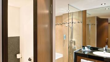 A modern bathroom with a glass-enclosed shower, a wooden vanity with a sink, and a toilet visible through an open door.