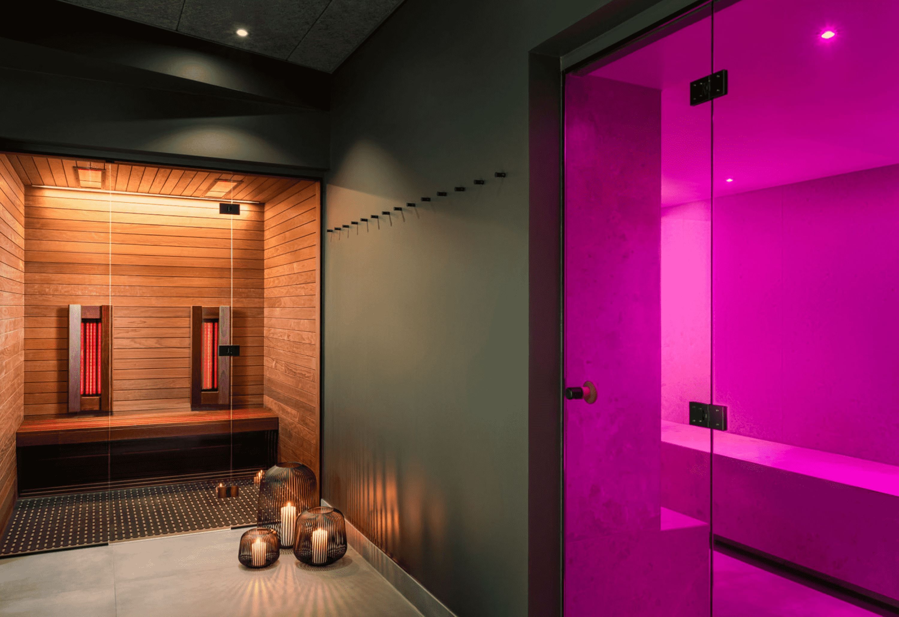 Ett modernt spa-rum med träpanel, uppvärmt golv och en bastu med rosa belysning.